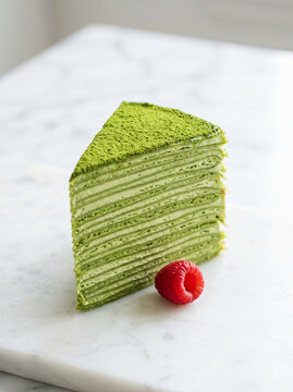 A single slice of delicious matcha green tea crepe cake served with a fresh raspberry on a marble surface.