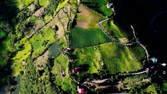 Aerial view of a densely built Andean town spread along a narrow valley, surrounded by steep green mountains and a winding river. Located in Tungurahua, Ecuador, the settlement&rsquo;s compact rooftops and 