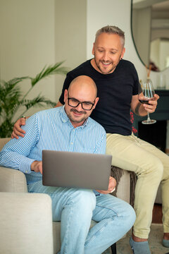 Mature same-sex partners browsing on a laptop and drinking wine at home
