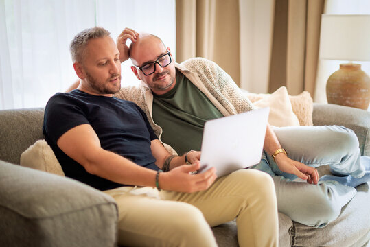 Same-sex male couple with laptop relaxing on a couch at home