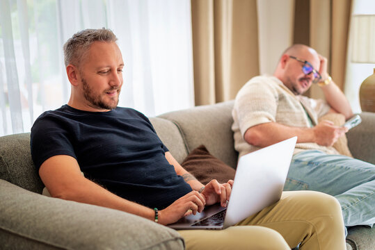 Same-sex male couple with laptop relaxing on a couch at home