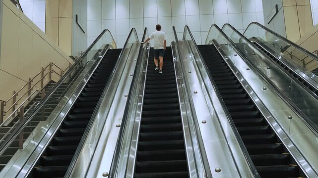 Male traveler rides upward on escalator inside modern metro station in Kuala Lumpur city, Malaysia. Public transportation, urban infrastructure, independent tourism, metropolitan mobility