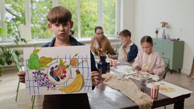 Portrait of Caucasian boy holding fruit painting in art class. Video ideal for promoting children education programs, creative development workshops and art masterclasses