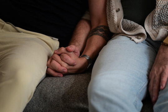 Close-up of a gay male couple holding hands while sitting together at home