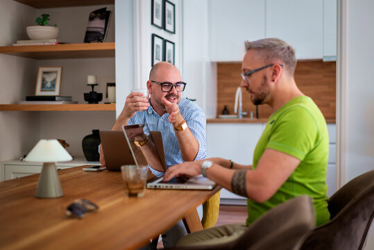 Same-sex male couple working from home, using a laptop together at the table