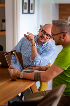 Same-sex male couple working from home, using a laptop together at the table