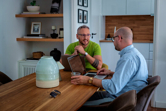 Same-sex male couple working from home, using a laptop together at the table