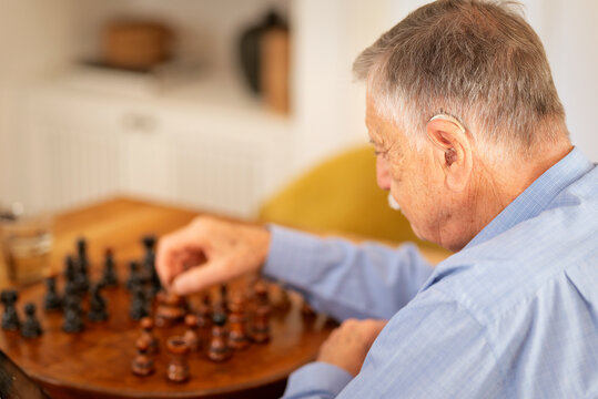 Elderly man sitting at a table and moving a chess piece on a wooden board