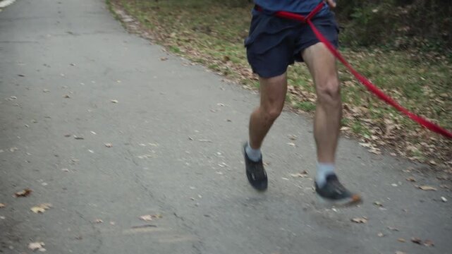 A man runs with a German Shepherd on a leash along a paved path in a forest park. The scene captures outdoor exercise, canine fitness and active bonding.