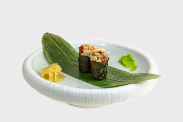 Two gunkan maki sushi with chopped eel and spicy sauce on bamboo leaf with wasabi and pickled ginger, white background © Evghenii Blanaru