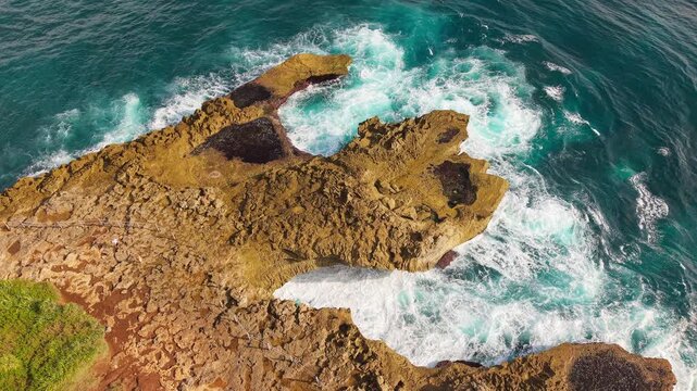 Waves crashing against volcanic cliffs at Devils Tears, Nusa Lembongan. Aerial view of turquoise water churning into white foam along rugged coast.