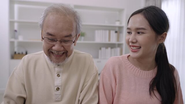 Happy beautiful Asian woman and her father are sitting smiling and playing piano, singing together having fun and cheerful in living room at home. Lifestyle and leisure after retirement with family. 