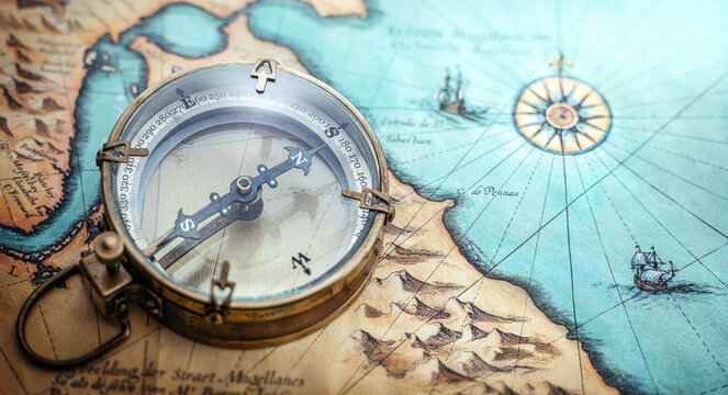 Vintage brass compass on an old geographic map close up. Antique navigation instrument for travel, exploration, geography and discovery concept. Adventure, tourism, cartography theme.