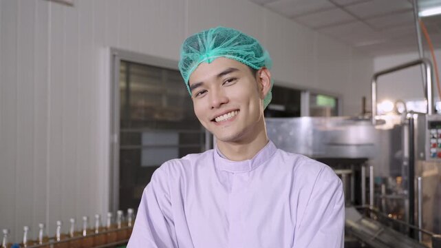 Happy Asian man technician inspector wearing glasses in a uniform of factory relaxing standing smiling with arms crossed while looking at the camera on a production line in the manufacturing industry.
