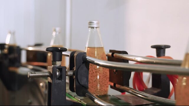 Fruit juice in glass bottles on an automated conveyor belt in modern beverage production facility line. Technology in the food and drink industry. Ready to drink fruit juice in manufacturing factory. 