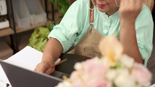 Asian senior woman, florist small business owner, entrepreneur feeling happy after getting order online at flower shop, independent pension lifestyle, creative workspace passion for business success
