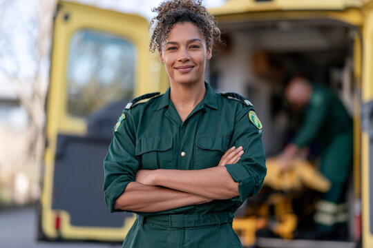 Confident female paramedic stands with folded arms beside an ambulance. Emergency service, medical professional, rescue team, public healthcare.