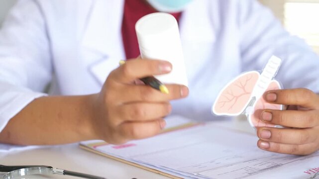 A doctor explains the effectiveness of medication for lung diseases, asthma, and bronchitis to a patient. He holds a medicine bottle and an anatomical model of the lungs on the clinic table. The conce