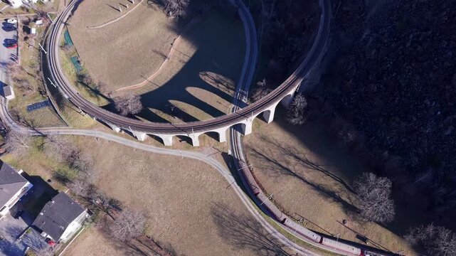 Aerial view of the iconic Bernina Express spiral viaduct in Brusio, featuring the curved stone bridge structure and railway tracks in Brusio, Grisons, Switzerland.