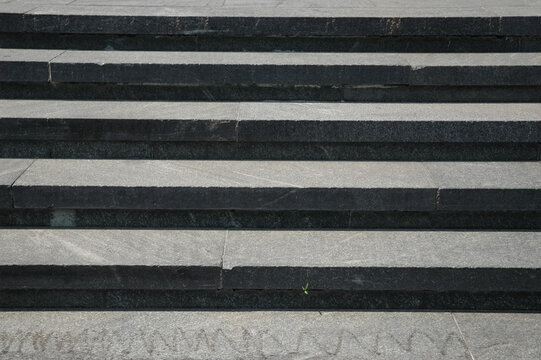 A straight front view of repeating wide grey granite stone steps under bright daylight.
