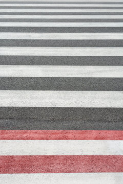 Full frame background texture of a street crosswalk painted with alternating horizontal stripes of textured red, white, and grey asphalt markings.