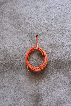A coiled orange corrugated plastic conduit pipe hanging from an opening on a grey textured stucco wall during building construction.