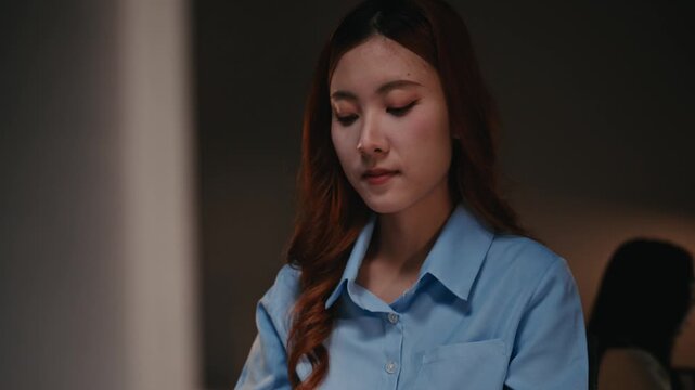 Dedicated Asian businesswoman concentrating on her work, typing on a computer keyboard while working late at night in a modern office, showcasing her commitment and professional work ethic