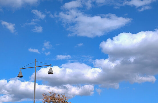 Clouds and a lamp post against a blue sky with some trees below in a park setting