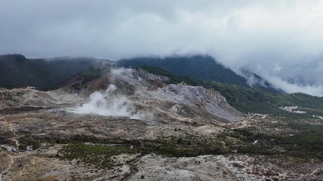 Aerial view of Mount Papandayan with active steam vents, rocky volcanic terrain, and lush mountain slopes under a cloudy sky in Garut, West Java, Indonesia.