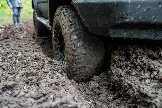 Mud packed tire sits deep in a churned vehicle rut with heavy tread pressed into soft soil, illustrating traction challenges and difficult access on unpaved driving routes