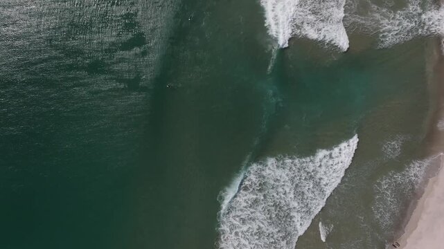 Aerial view of ocean waves breaking along the sandy coastline of Whiritoa, New Zealand.