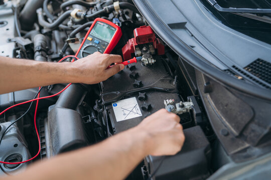 Top view of a mechanic checking car battery voltage with a multimeter