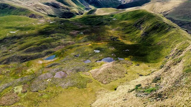 Drone footage presents a wide aerial view of a blue reservoir enclosed by rugged Andean mountains in Ecuador. An embankment dam, curving access roads, small buildings, green highland slopes and cloud 