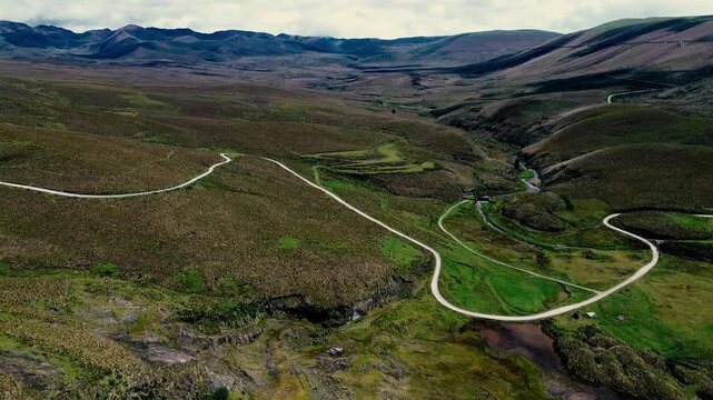 Aerial footage over the Ecuadorian Andes reveals small reflective ponds scattered across a broad highland wetland, surrounded by rolling green and golden hills. Patchy grasses and wetland vegetation c
