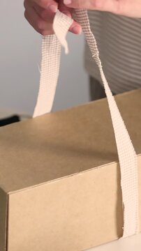 Hands tying gingham ribbon bow around kraft cardboard gift box for Christmas