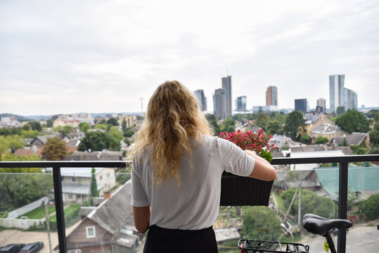 A Woman Watering Flowers on her Balcony Overlooking Traditional Wooden Houses and Modern Skyscrapers in the Heritage Neighborhood of &Scaron;nipi&scaron;kės in Vilnius, Lithuania