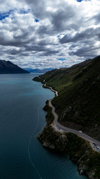 Aerial view of the winding Devils Staircase road along the rugged coastline of Lake Wakatipu, featuring steep green hills and deep blue water in Devils Staircase, Otago Region, New Zealand.
