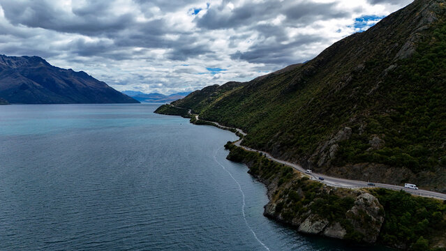 Aerial view of the Devils Staircase winding road along the edge of Lake Wakatipu with rugged mountains and cloudy sky in Devils Staircase, Otago Region, New Zealand.