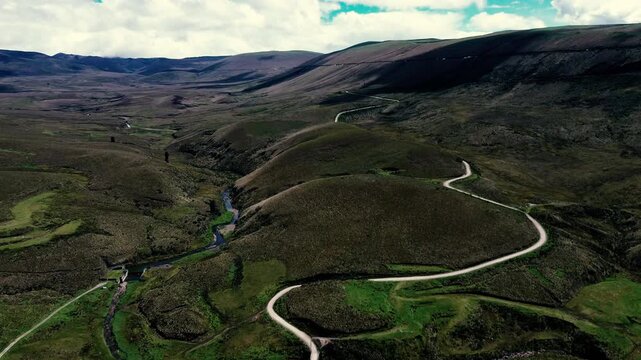 Overhead drone footage of an Andean wetland in Ecuador, where green and yellow vegetation forms a varied ground pattern around dark pools and winding water channels. The broad aerial composition revea