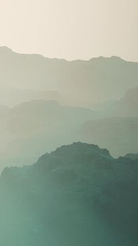 At sunrise, layers of mountains appear shrouded in mist. The scene shows the soft outlines of the hills in the distance. This place has a quiet and distant feel.