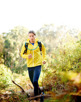 Running, athlete and man with earphones, forest and active with backpack in nature, wellness and music. Outdoor, runner and person with tech for playlist, energy and listening to radio for exercise