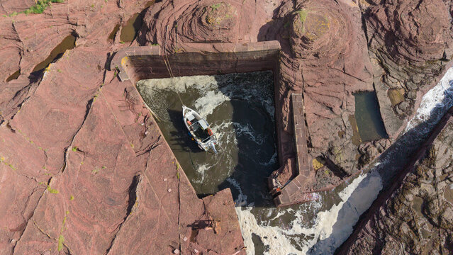 Aerial view of a boat in the historic and tiny Seacliff Harbour carved into red sandstone rock in East Lothian Scotland. This unique landmark is known as the smallest harbor in the UK.