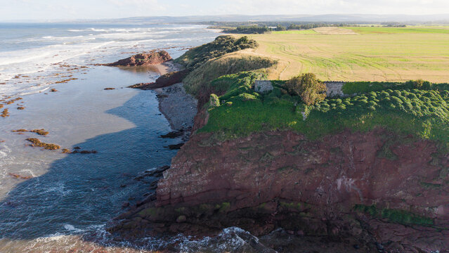 Historic ruined stone tower and walls of Seacliff standing on edge of steep red sandstone cliff overlooking sea in East Lothian Scotland