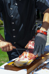 Fototapeta premium Corte de jamón serrano tradicional español con guante protector. Gastronomía tradicional española; tallado de jamón ibérico; chef profesional en cocina gourmet.