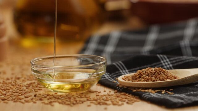 Sesame oil pouring into glass bowl on flax seeds, light Asian sesame like flaxseed, sunflower or extra virgin olive oil, healthy cooking ingredient macro close up