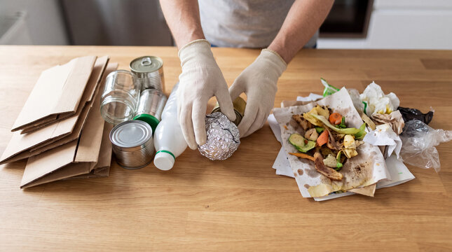 Person wearing gloves separating various types of garbage on a wooden table, preparing items for reuse and disposal
