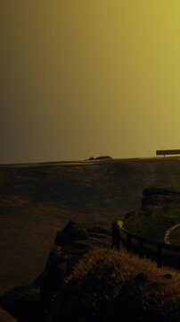 A person stands near a railing at a high location during sunset. The sky is a mix of colors. Distant hills are visible in the background.
