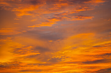 Fototapeta premium Dramatic cloudy sky at sunset glowing with intense orange and golden light, colorful evening clouds and atmospheric natural background 