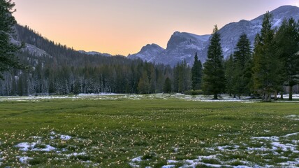 Naklejka premium Snow-dusted mountain meadow beneath a serene alpine sunset