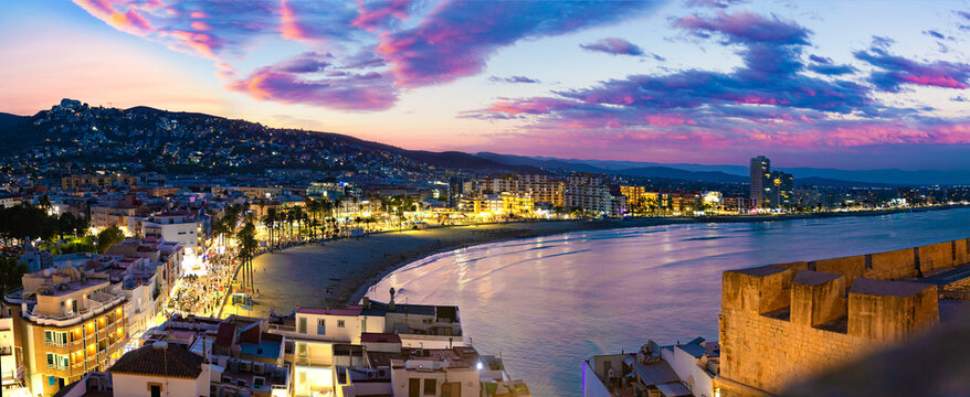  Vista panor&aacute;mica nocturna de la ciudad costera iluminada de Pe&ntilde;iscola. Ciudad costera de noche; playa iluminada y fortaleza hist&oacute;rica bajo el cielo crepuscular.